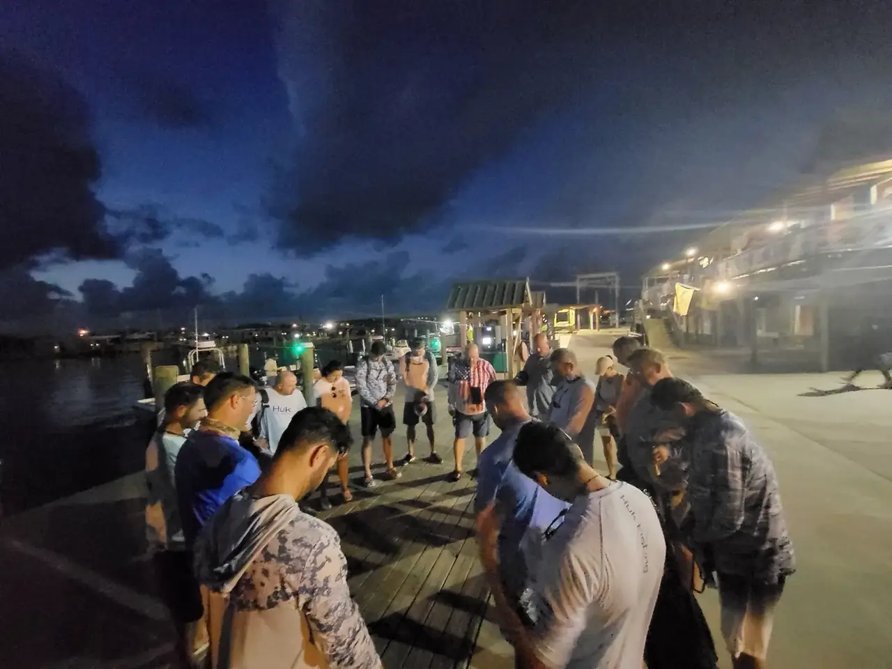 Guests standing in a circle with heads bowed on the dock at Venice Marina before dawn