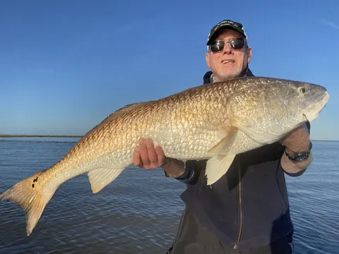 Angler in a dark jacket holding a redfish under a clear blue sky near Venice, Louisiana