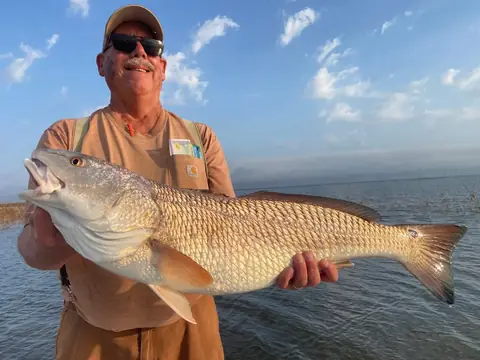 Angler in a tan shirt holding a redfish over open water near Venice, Louisiana