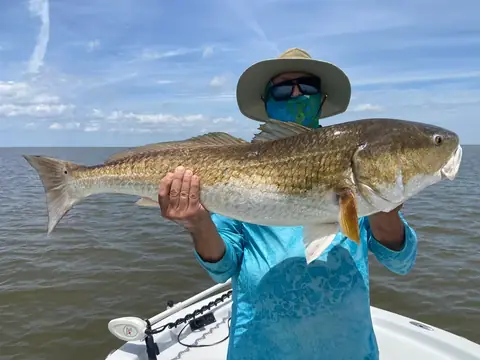 Angler in a teal shirt and sun hat holding a redfish out in front of him near Venice, Louisiana