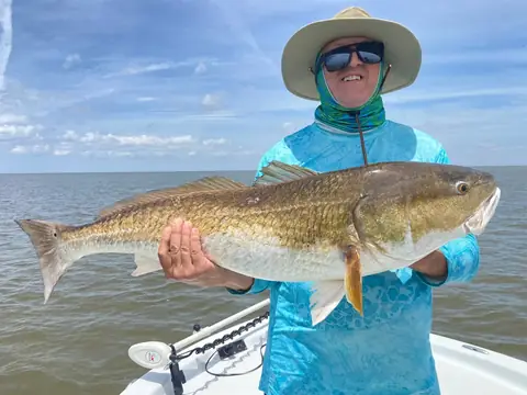 Angler in a teal shirt and sun hat holding a redfish on the bow near Venice, Louisiana
