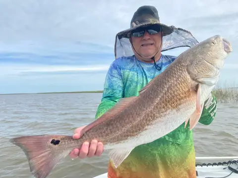 Angler in a tie-dye shirt and sun hat holding a redfish near Venice, Louisiana
