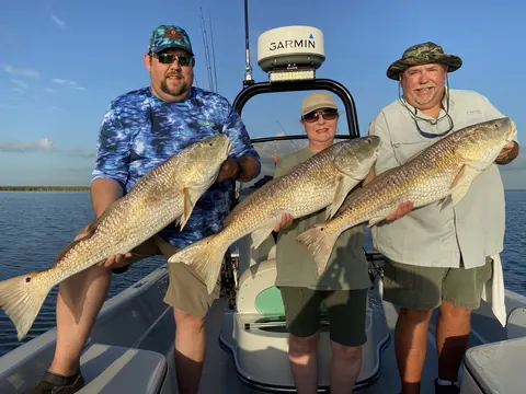 Three anglers each holding a redfish on the boat in evening light near Venice, Louisiana