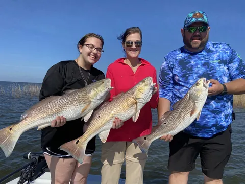 Three anglers on the boat each holding a redfish near Venice, Louisiana