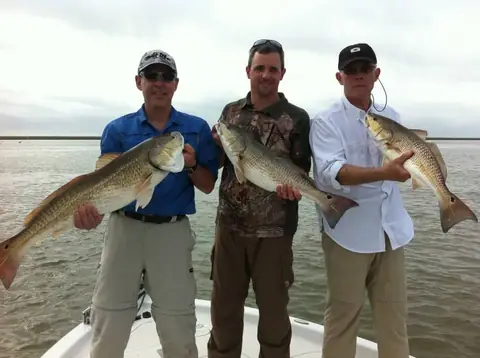 Three anglers standing on the bow, each holding a redfish
