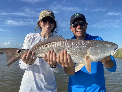 Two anglers holding a redfish between them under a blue sky near Venice, Louisiana