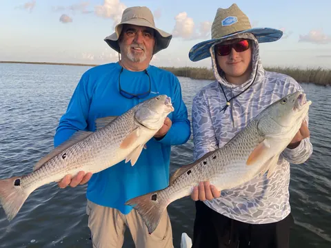 Two anglers in sun hats each holding a redfish near Venice, Louisiana