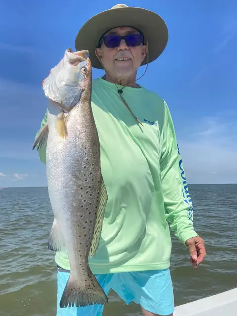 Angler holding a large speckled trout on a bright day